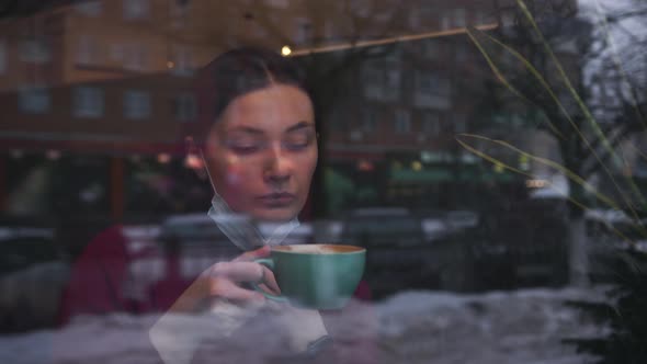 A Woman is Drinking Coffee in a Cafe Wearing a Mask