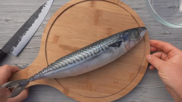 Top View of the Male Hands Putting the Mackerel Fish on the Round Wooden Board