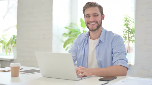 Young Creative Man with Laptop Smiling at Camera