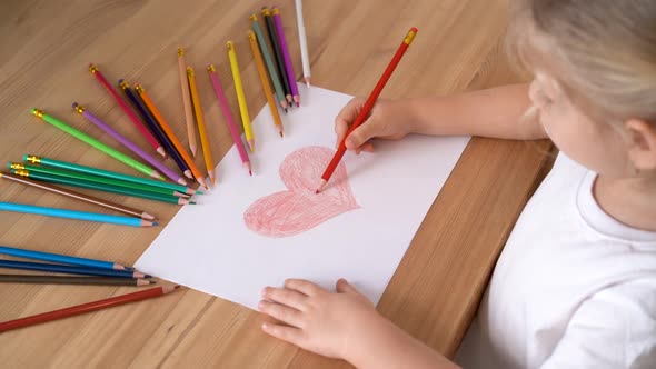 the Hands of a Small Child Draw a Heart with a Red Pencil on a White Piece of Paper