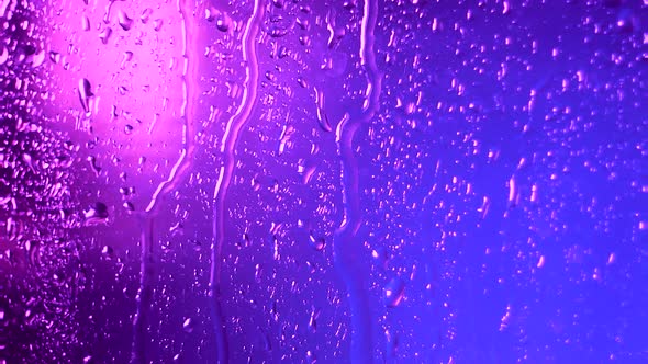 Raindrops of Water Flow Down the Glass in Rainy Weather on a Colored Pink Blue Blurred Background