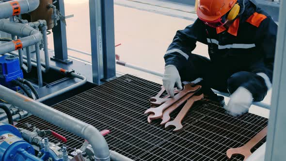 A Mechanic in a Helmet Goggles and Headphones Prepares a Working Tool Copper Wrenches for alt