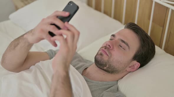 Beard Young Man Scrolling on Smartphone in Bed