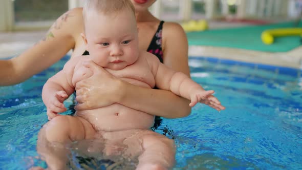 Happy Mother in Red Swimming Suit with Baby Son Surfing Water with Fun in Swimming Pool