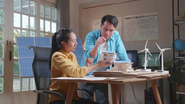 Asian Man And Woman Helping Each Other Building The Model Of A Small House With Solar Panel