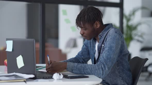 Side View of Stressed Man Crumpling Paper Sitting at Table in Home Office