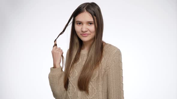 Smiling Young Teenage Girl Twisting Long Hair on Finger and Looking in Camera