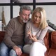 Hilarious Mature Couple Sitting on the Sofa and Holding Smartphone - VideoHive Item for Sale