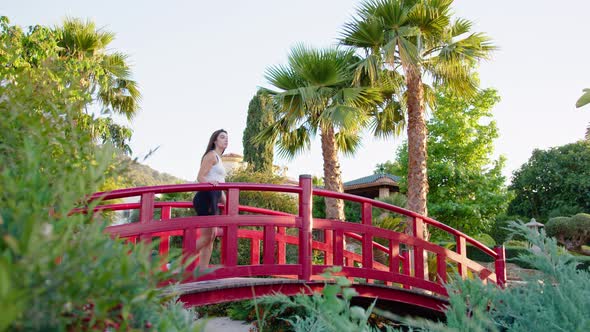 Wide shot of a young woman walking over a bridge and stopping to look around