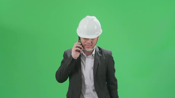 Asian Chief Engineer In The Hard Hat Talking On Mobile Phone While Walking On Green Screen