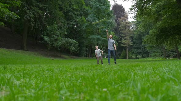 Dad and Son Together Launch Model Airplane Outdoors, Both Man and Boy Are Looking Cheerfully at