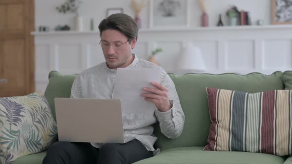 Man  with Laptop Reading Documents on Sofa