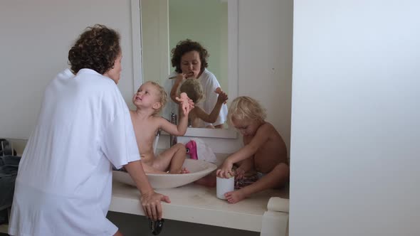 Mom with Children in the Bathroom Brushes Her Teeth in the Morning