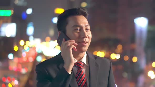 Asian young business man smiling with happiness and talking on smartphone outdoor in city at night.