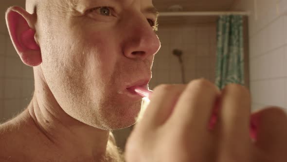 A man brushes his teeth towards a bathroom mirror