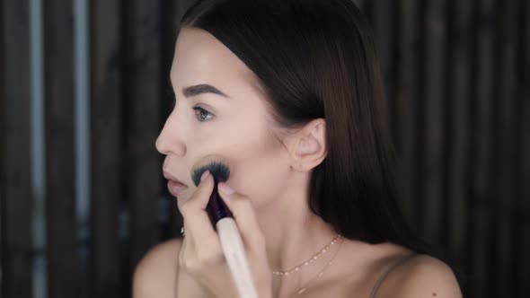 Beautiful Young Wellgroomed Woman Applies Shadows and Highlighter