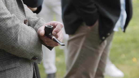 Man in Business Suit Stands on Lawn and Holds Wooden Smoking Pipe in His Hand