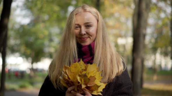 Portrait of Happy Charming Caucasian Young Woman Posing with Leaves Bouquet in Autumn Park