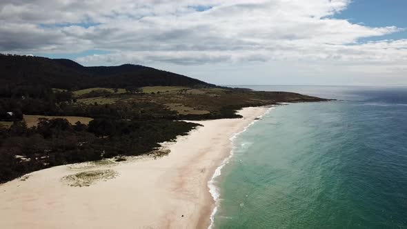 Drone Pan Over White Sand Beach Surrounded By Trees With Waves Rolling In, Tasmania Australia