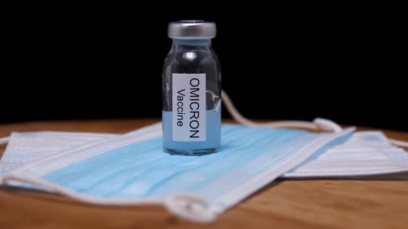 Close-up of Omicron vaccine vial and medical masks against a wooden background