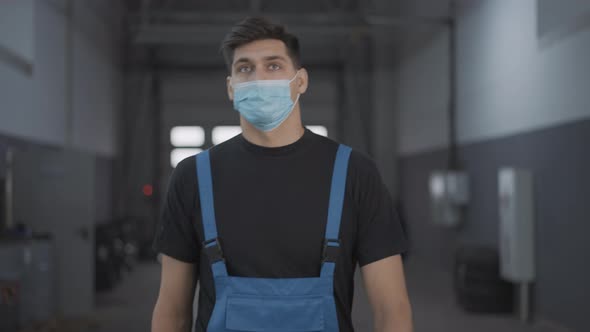 Portrait of Young Confident Man in Covid Face Mask and Uniform Walking in Repair Shop Looking Around