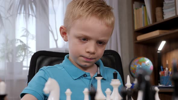 Portrait of a Little Boy Playing Chess at Home at the Table