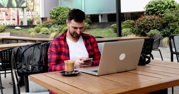 Handsome young businessman using a laptop and a smartphone.