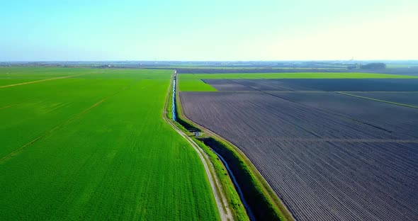 Irrigation Canal Divides Green Field and Plowed Terrain