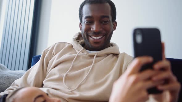 Close Up Of Woman Resting On Partners Lap At Home On Sofa Checking Social Media On Mobile Phone