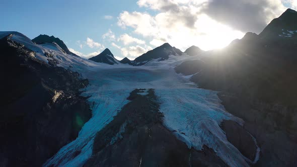 Aerial closeup sliding by snow-capped mountain peak against shining sun in summer Alaska