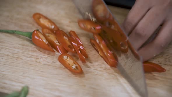 Cutting a Red Chili Pepper into Slices with Knife on Wooden Chopping Board - Close Up