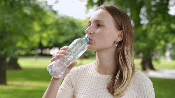 Portrait of Young Beautiful Woman Drinking Water at Summer Green Park.