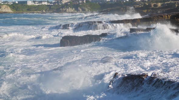 Tumultuous ocean waves crashing into rocks, shooting water straight up into the sky.