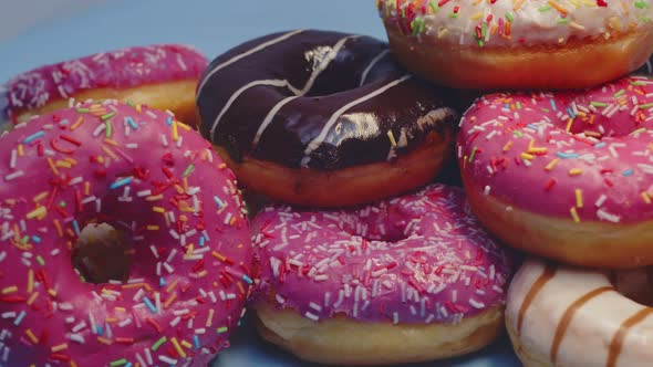 Lot of Fresh Delicious Donuts with Multicolored Glaze Lie on Blue Background Closeup