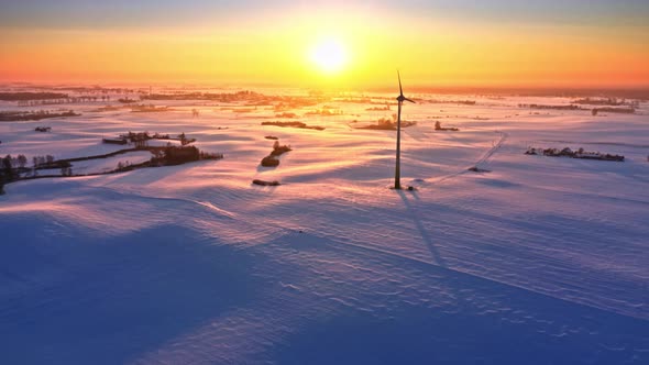 Snowy field and wind turbine at winter sunrise. Alternative energy