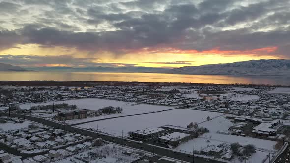 Aerial view flying backwards over snow covered urban city landscape at sunset