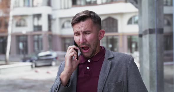 Portrait of Man Talks on the Phone and Sneezes Strongly Near Office Centre