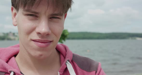 Handsome Young Man Looking Into Camera and Corrects Hair Outdoors