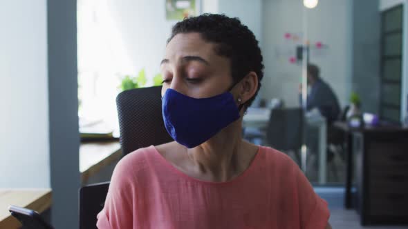 Caucasian woman wearing face mask sneezing on her elbow at modern office