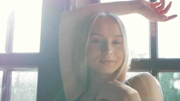 fashion portrait of a beautiful young woman with blue eyes and blonde hair poses near the window