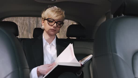 A Businesswoman in Glasses Is Working in a Car