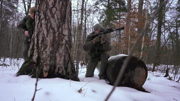 Group of Armed Caucasian Young People in Winter Forest Outdoors Hiding Aiming in Slow Motion