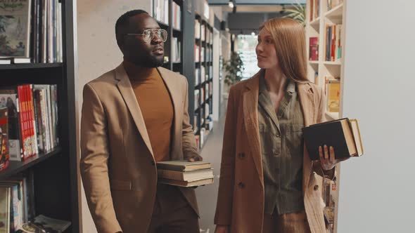 Modern Interracial Couple Walking along Bookshelves in Library