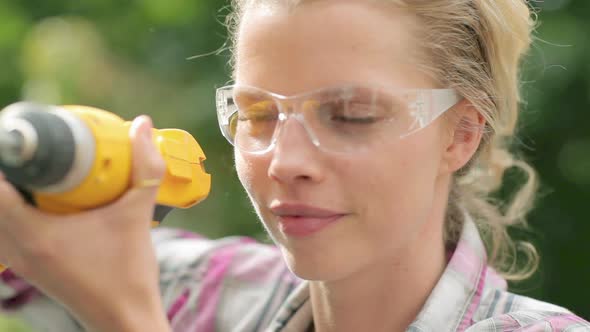 Woman wearing safety goggles with electric drill