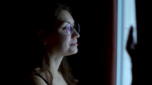 smiling woman in glasses walks to the window, opens the curtain and looks out.