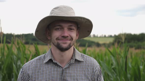 Close Up of Young Smiling Farmer in Hat Looking Into Camera Against the Blurred Background of Corn