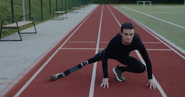 Strong Young Male Sportsman with Prosthetic Running Blades Stretching Limbs at Sports Field