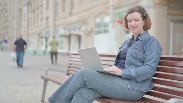 Old Woman with Laptop Showing Thumbs Up Sign While Sitting Outdoor on Bench