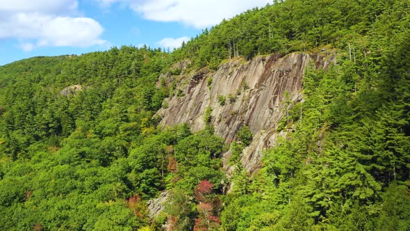 Aerial footage PUSH in towards forested cliff with lone climber in blue