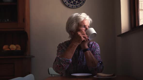 Woman drinking coffee on dining table in kitchen at home 4k